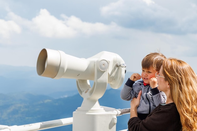 Mother shows son landscapes in valley of Rhodope Mountains and sky through telescope on observation tower of Snezhan