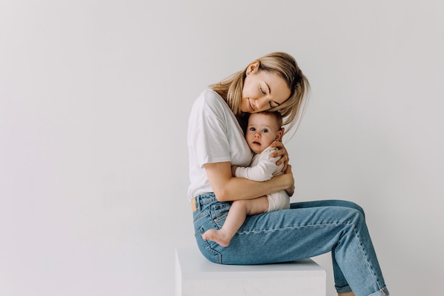 Mother sitting and hugging her baby on white wall background