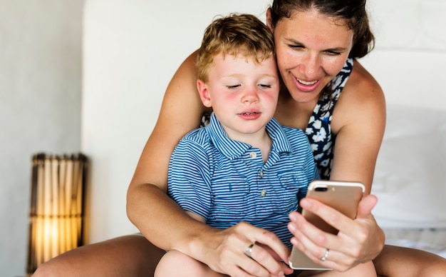 Photo mother sitting with son on bed using mobile