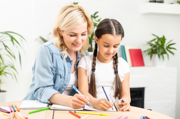 mother and small 8s daughter at home have fun painting together with colors. Happy mom or nanny and little girl child enjoy drawing. Hobby concept