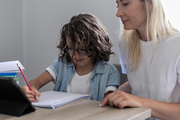 Mother and small son eyeglasses study online on tablet at home together lesson prepare homework