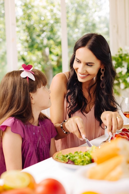 Mother smiling while giving salad for her daughter