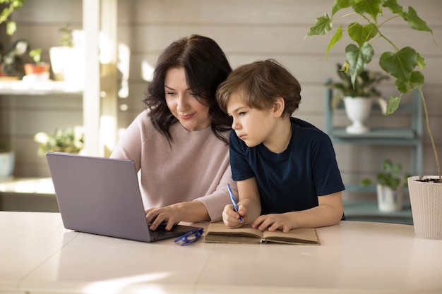 Mother and son are engaged in online school sit in a laptop and make notes in a notebook