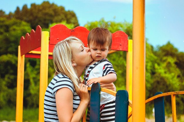 Mother, son are playing in playground, laughing on summer walk. sunny day.  Family holiday. Kids