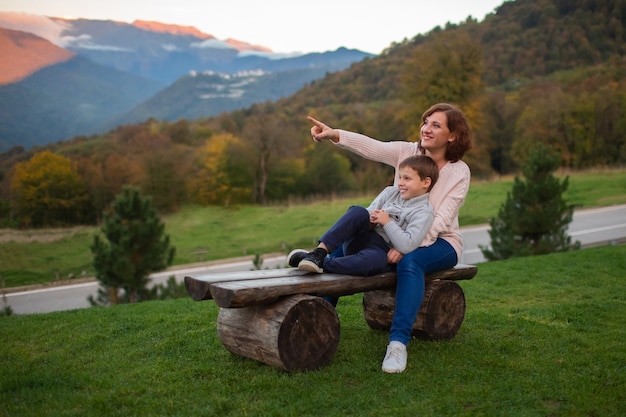 mother and son are sitting on wooden benches in the mountains