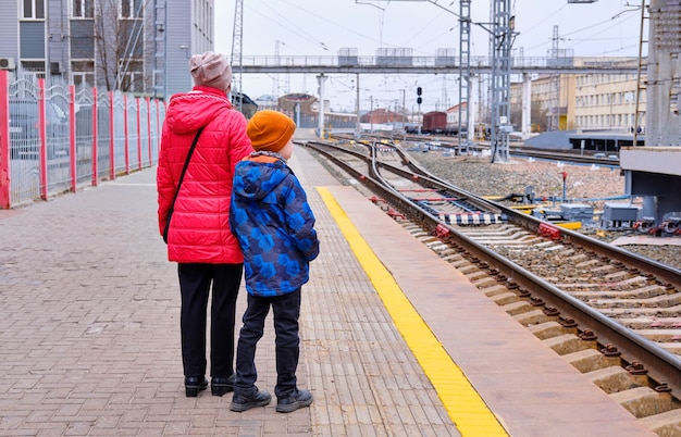 Mother and son are walking along the platform of the station and waiting for the train