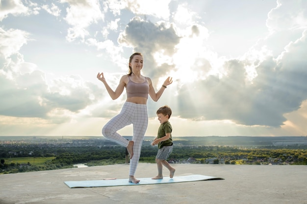 Mother and son doing exercise on the balcony in the of a city during sunrise or sunset