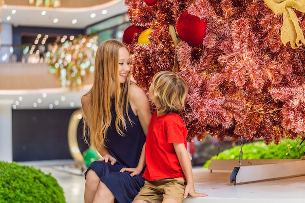 Mother and son hangs a decoration on the red Christmas tree