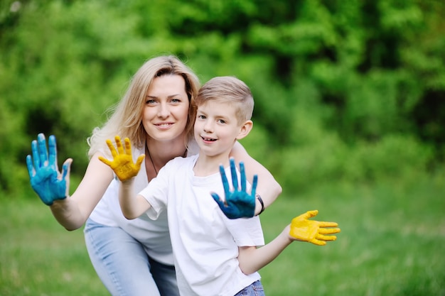 Mother and son playing on the background of green trees. Mom and son hands smeared with colored paint.