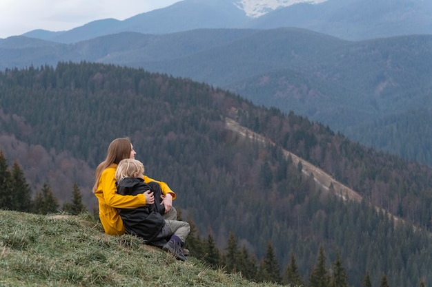 Mother and son rest and sit in an embrace on mountains background Young mother with son sit on hillside