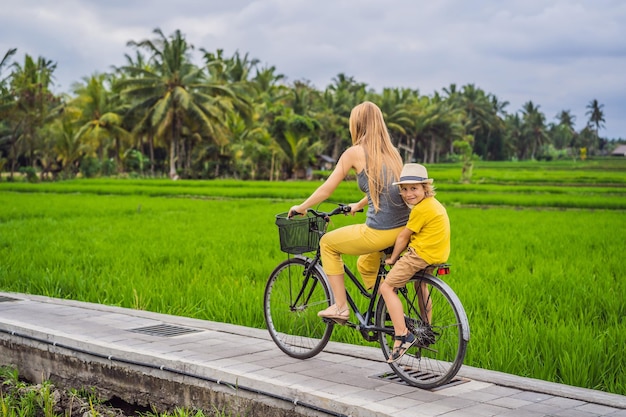 Mother and son ride a bicycle on a rice field in ubud bali travel to bali with kids concept