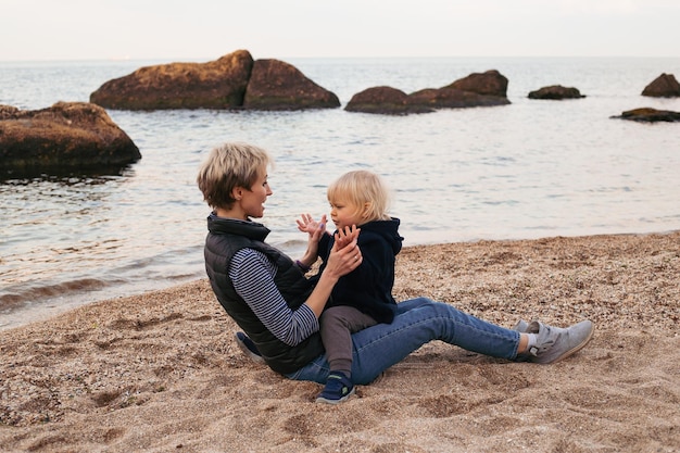 Mother and son sitting and have a fun near the sea in autumn time