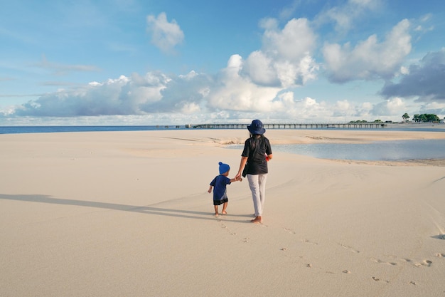 A mother and son walk on the beach in front of the pier.