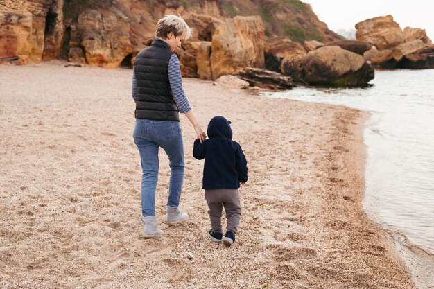 Mother and son walking on beach near sea in autumn beach