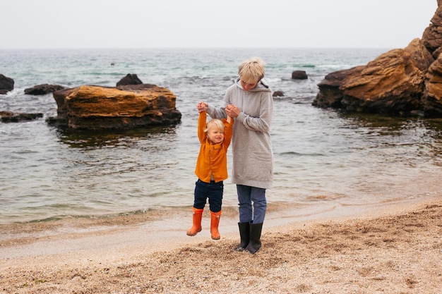 Mother and son walking on beach near sea in autumn beach