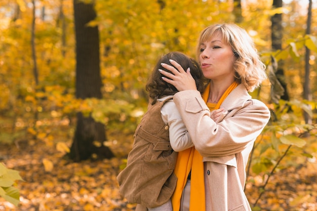 Mother soothes her crying blonde daughter mom holds sadness baby in her arms in autumn nature