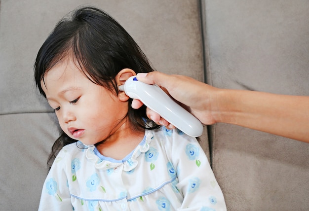 Mother takes temperature for her daughter with ear thermometer at home