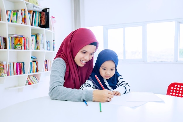 Mother teaching her daughter to write on a book