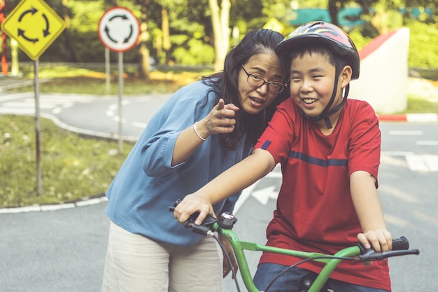 Mother teaching her sun to ride bicycle in park. Family outdoor on bike ride.