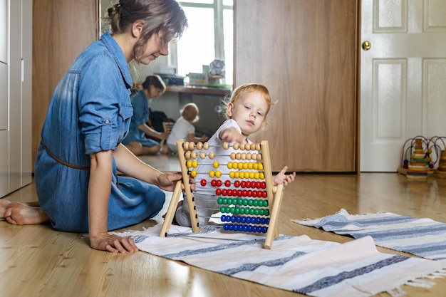 Mother teaching little kid counting on multi colored childish wooden ecological abacus on floor