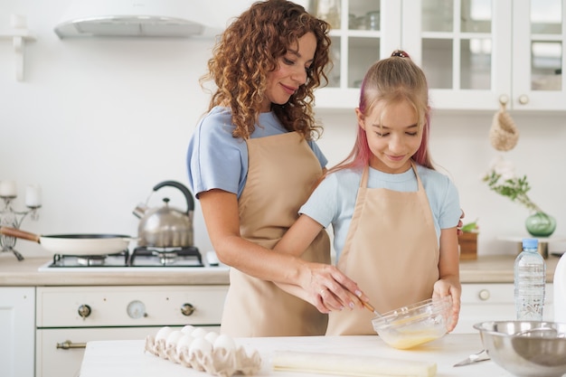 Mother and teen daughter making dough for pastry toghether in kitchen