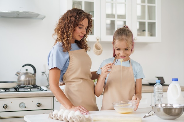 Mother and teen daughter making dough for pastry toghether in kitchen