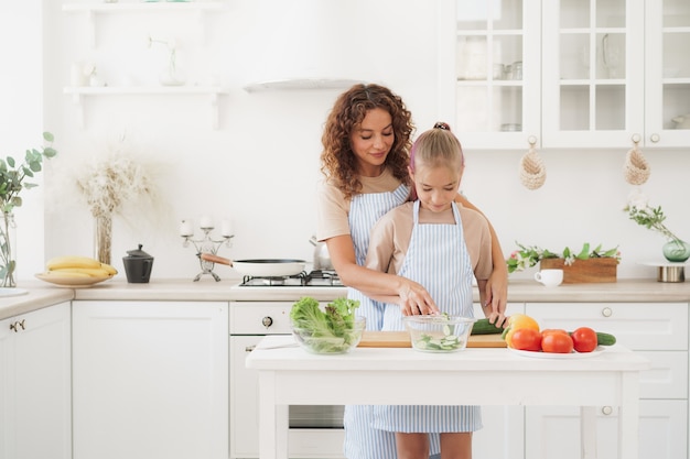 Mother and teen daughter preparing vegetable salad at kitchen