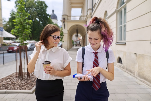 Mother and teenage daughter walking together on city street. Talking mom and girl student, parent and child discussing school, study