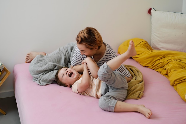 Mother tickling child in bed playing in the morning