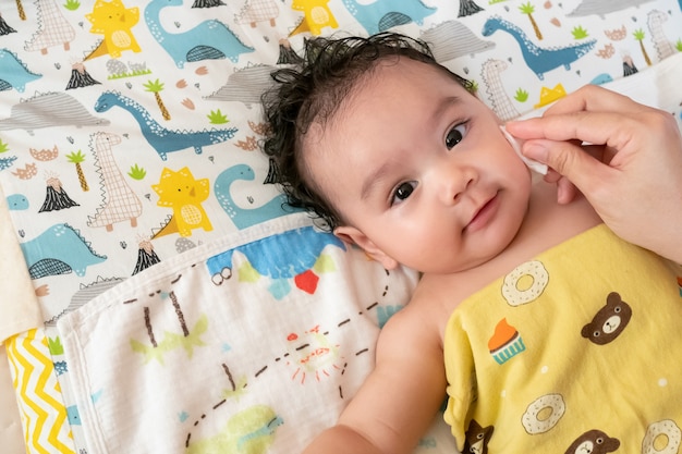 Mother uses a cotton swab moistened with clean water. Clean Asian baby face after bathing, little cute baby look at camera