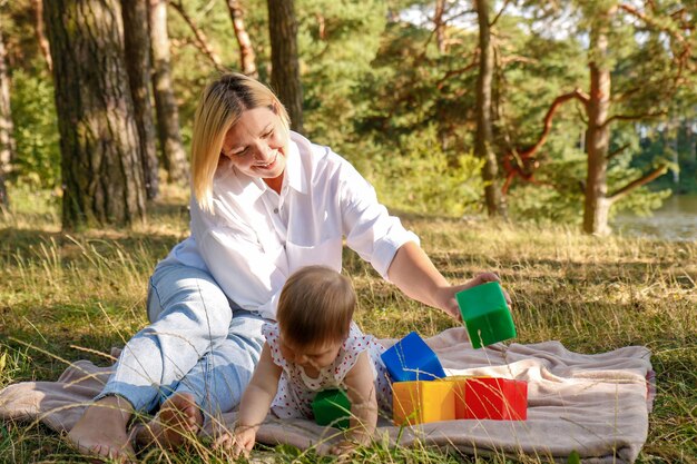 mother with baby daughter play with blocks in the park on a sunny day