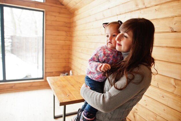 Mother with baby girl in hands at modern wooden house spending time together in warm and love