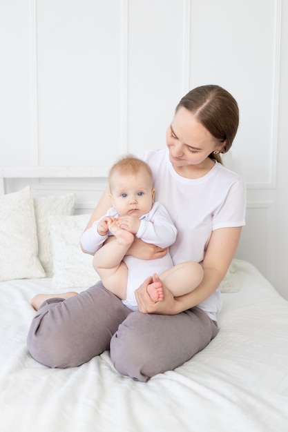 A mother with a baby in her arms gently hugs a child on the bed at home