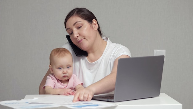 Mother with baby on lap talks on phone analysing report