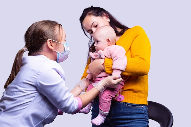 A mother with a baby on a medical inspection a young doctor is examines a baby in a mask and uniform