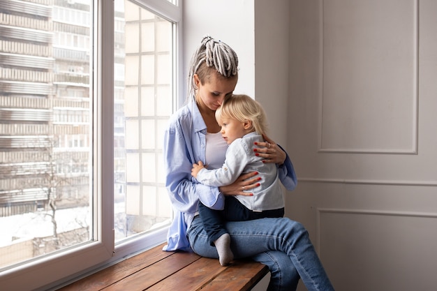 Mother with baby son sitting by the window and playing