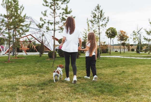 A mother with a child and a dog Jack Russell terrier are walking together in the park a woman and a little girl are walking their dog