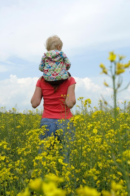 Mother with child on a yellow field in bloom with blue sky and white clouds