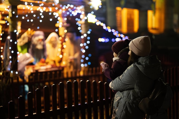 Mother with daughter against scene where the Virgin Mary gave birth to Jesus and he lies in the cradle surrounded by people who have come to celebrate the Nativity of Christ