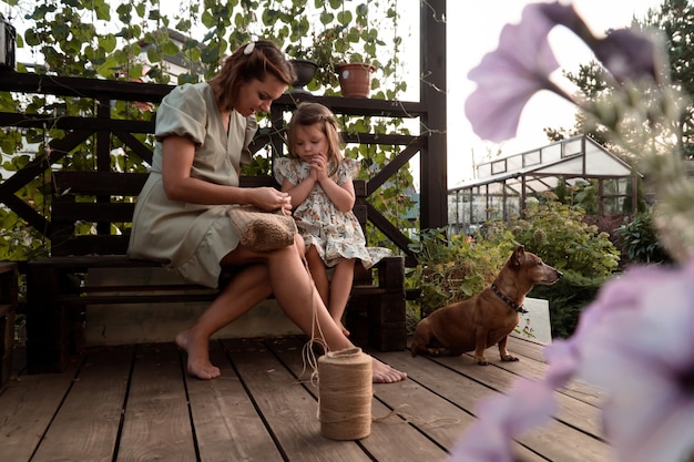 mother with daughter crochet eco bag from jute yarn outdoors on wooden terrace of country house