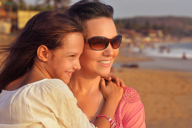 Mother with daughter hugging on sandy beach during sunset