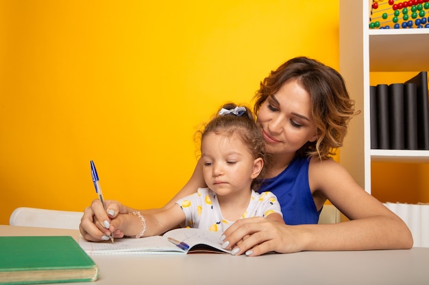 Mother with daughter studying together sitting at the table at home isolated.