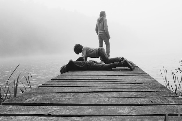 Photo mother with daughters on pier at lake during foggy weather