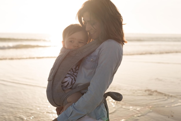 Mother with ergobaby carrying toddler on the beach