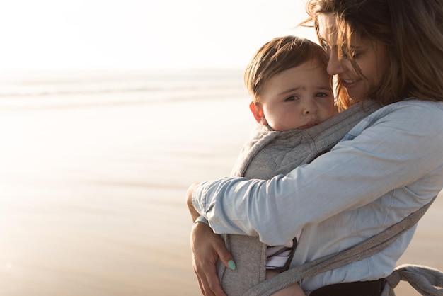 Mother with ergobaby carrying toddler on the beach