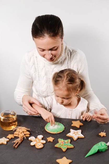 Mother with girl decorating gingerbread cookies for christmas