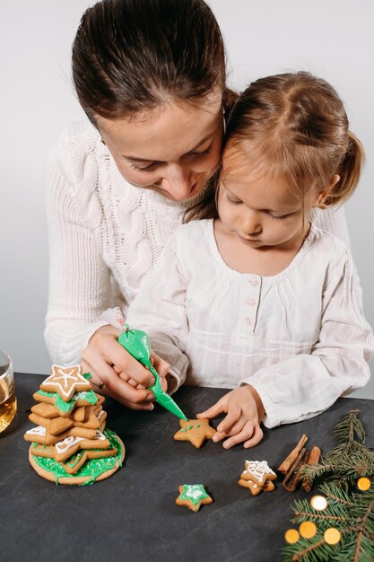 Mother with girl decorating gingerbread cookies for christmas