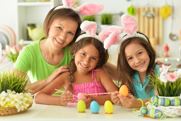 Mother with girls wearing rabbit ears decorating Easter eggs