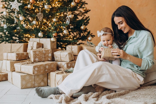 Mother with her baby daughter with gift boxes by the Christmas tree