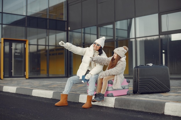 Mother with her daughter sitting outdoors on a luggage and waiting for travel